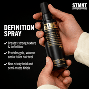 Two Hands holding a STMNT Definition Spray bottle with product details on a black background Primos Barber Supply