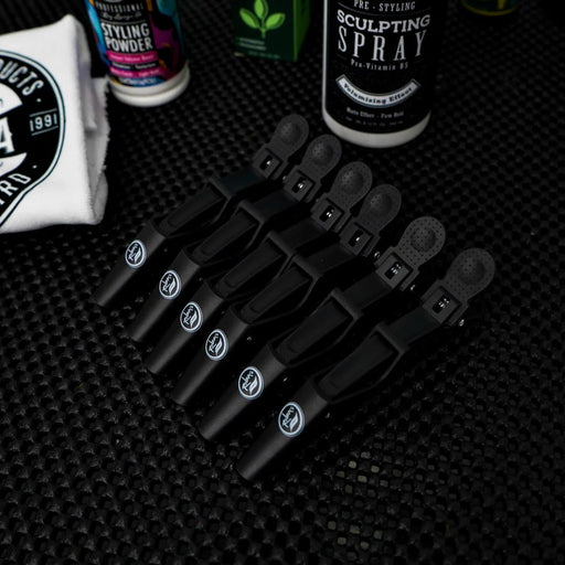 Set of black hair clips on a textured black surface with styling products in the background.