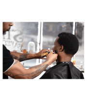 Barber using clippers on a customer's head in a salon setting.