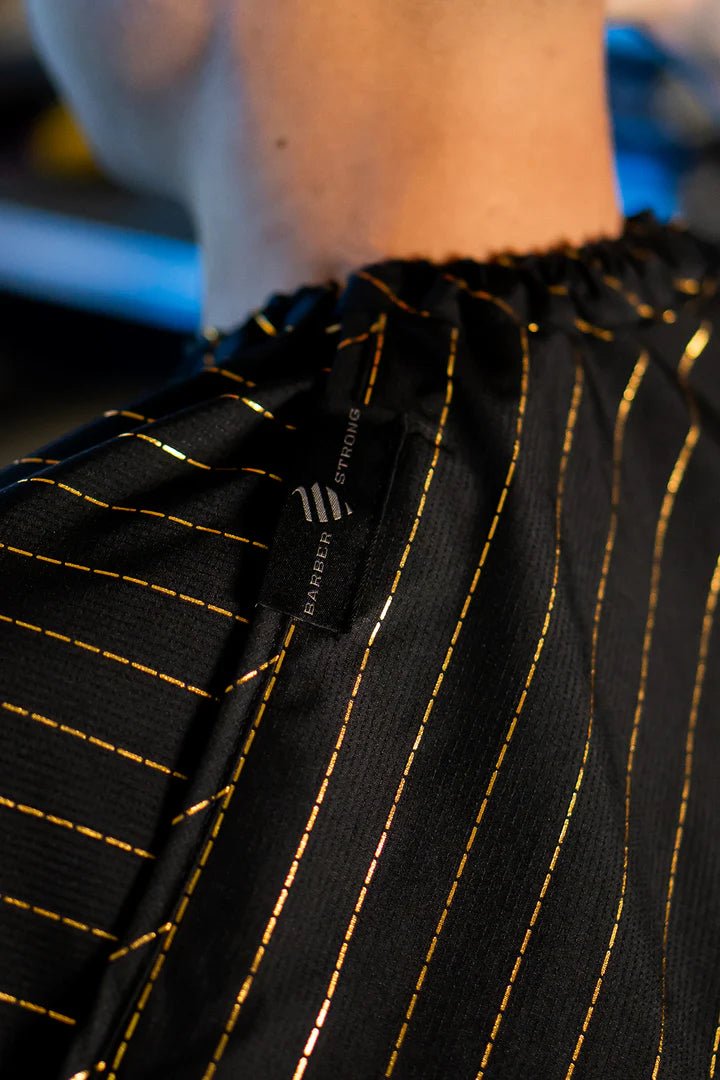 Barber Strong Shield Collection black barber cape with 24K gold pinstripes neck closure detail