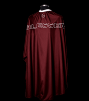 Blessed Capes Bordeaux barber cape in a solid maroon color featuring lightweight water-resistant material and full professional coverage for barbers and stylists.
