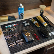 Black Gamma+ Professional Barber Mat with clippers and shears organized on a station.