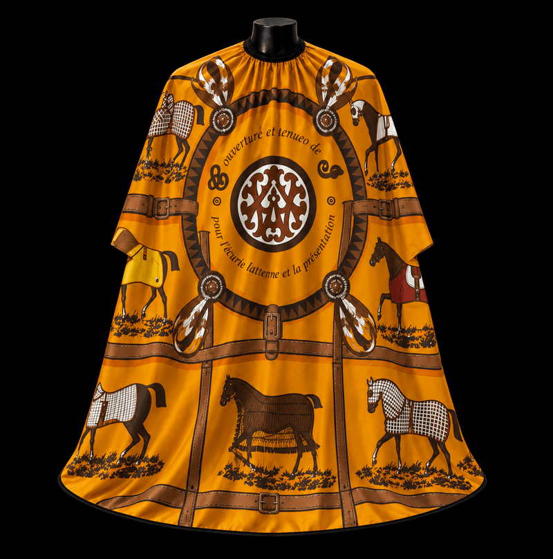 Hermes Orange Barber Cape - front-facing view showing the equestrian toile print with illustrated horses and a central medallion on a golden-orange lightweight water-resistant polyester cape