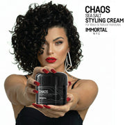 Woman with defined curls holding an open jar of Immortal NYC Chaos Sea Salt Curl Cream