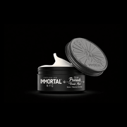 Open jar of Immortal NYC cream pomade with black lid on a black background