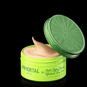 Green jar of 'Immortal NYC' styling product with open lid on a black background