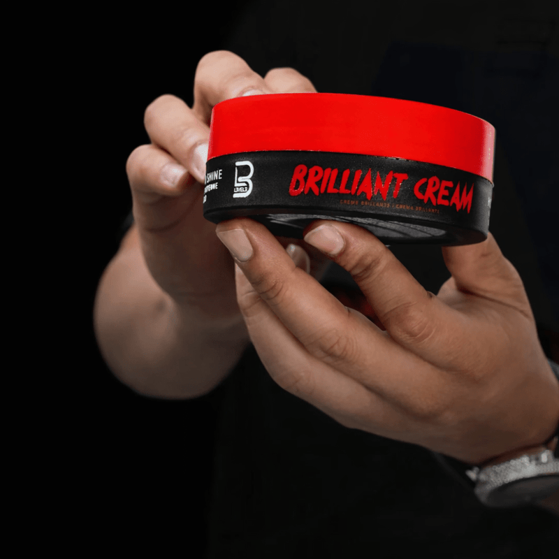 Hand holding a container of Brilliant Cream against a black background