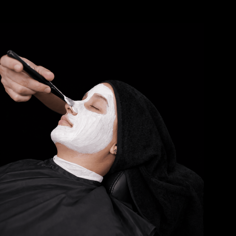 Person getting a facial mask applied in a black background 