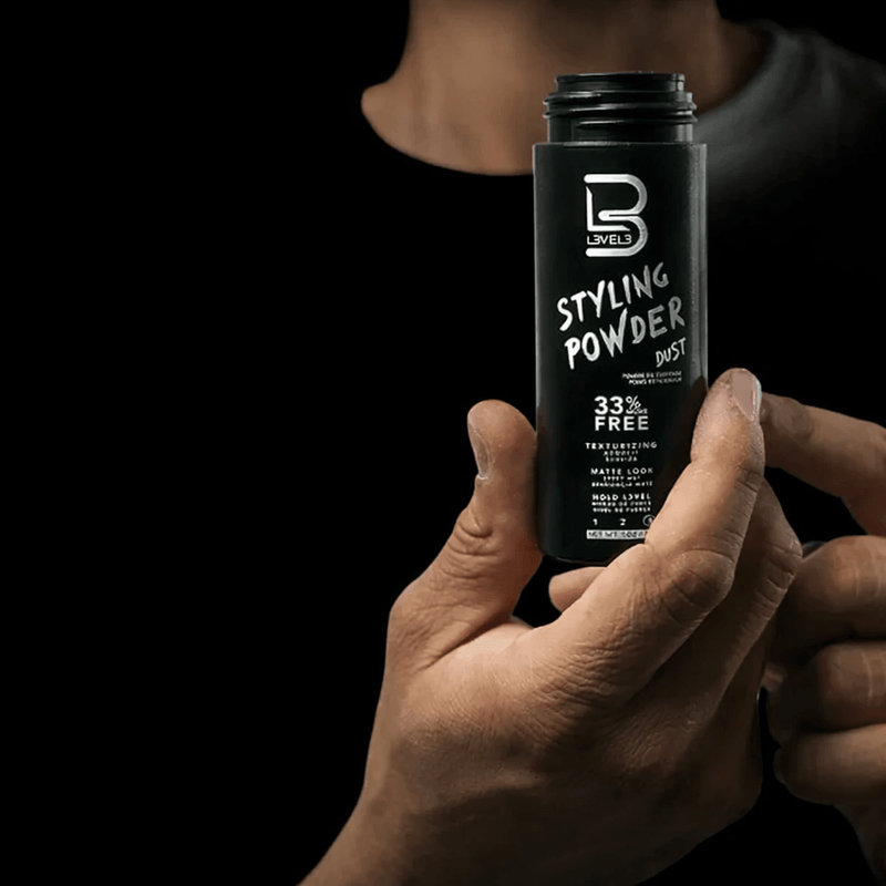 Hand holding a bottle of L3VEL3 Styling Powder against a black background