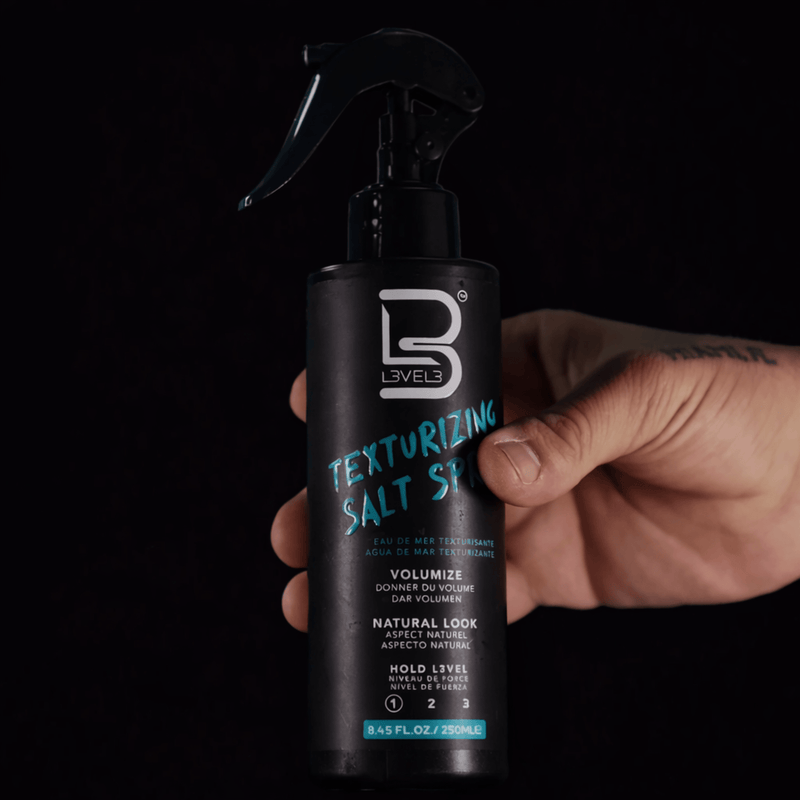Hand holding a black spray bottle labeled 'Texturizing Salt Spray' against a dark background