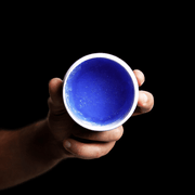 Hand holding a purple container showing the top of the jar that look like clear jelly against a black background. Primos Barber Supply