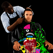 StyleCraft Radioactive Black Barber Cape in use during haircut on black background for Primos Barber Supply
