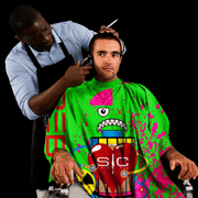 StyleCraft Radioactive Green Barber Cape in use during haircut on black background for Primos Barber Supply