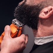 Barber using the StyleCraft Saber 2.0 orange clipper to shape a client's beard line