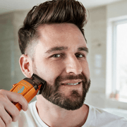 Smiling bearded man trimming his beard with the StyleCraft Saber 2.0 orange clipper